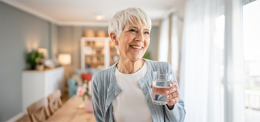 A senior woman smiling with a glass of water.
